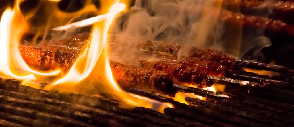 Traditional Adana Kebab sizzling on skewers over hot coals with rising smoke and flames.